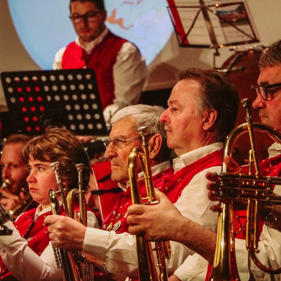 Eine Gruppe von Musikern in roten Westen spielt Trompeten und Posaunen bei einem Konzert.
