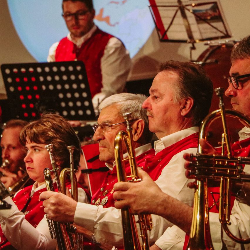 Eine Gruppe von Musikern in roten Westen spielt Trompeten und Posaunen bei einem Konzert.