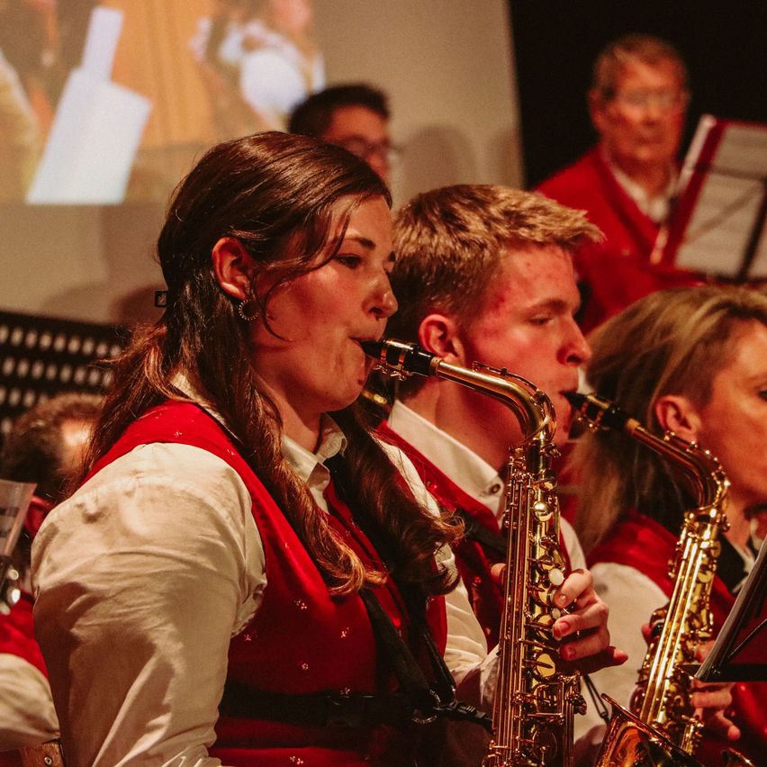 Eine Gruppe von Musikern, die Saxophon spielen, einschließlich einer Frau vorne, bei einer Veranstaltung in Innenräumen.