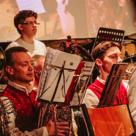 Eine Gruppe von Musikern tritt bei einem Konzert auf. Sie stehen vor ihren Instrumenten, und der Mann links hält ein Blechblasinstrument.