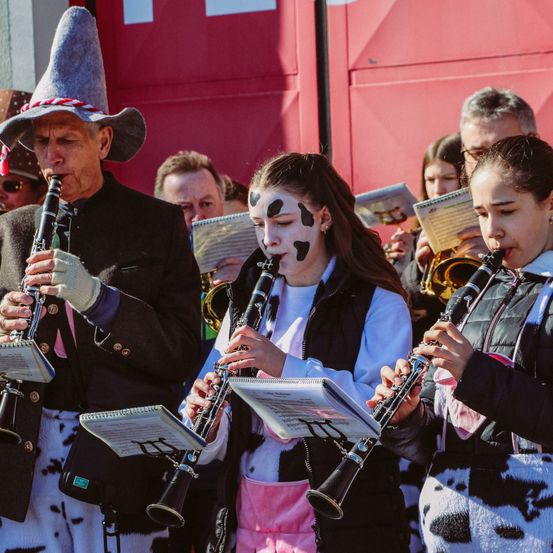 Eine Gruppe von Musikern spielt im Freien, einer in einem Cowboy-Kostüm, zwei Mädchen in Kuhkostümen und einer anderen mit einer Trompete.