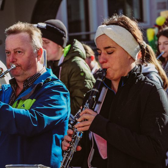 Ein Mann in einer blauen Jacke spielt Trompete, während eine Frau Klarinette spielt bei einer Veranstaltung im Freien.
