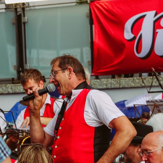 Ein Mann in einer roten Weste singt in ein Mikrofon vor einer Menschenmenge.