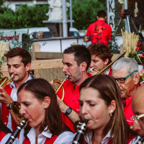 Eine Gruppe Musiker, die rote Hemden und weiße Hemden mit Kragen tragen, spielt auf der Bühne ihre Instrumente.