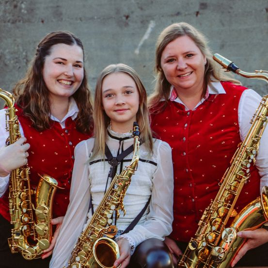 Drei Frauen mit Saxophonen; eine lächelt, eine posiert und die andere hält ein Saxophon.