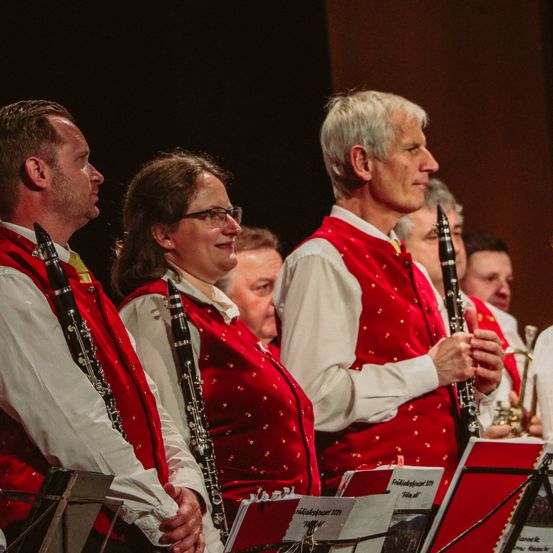 Eine Gruppe von Musikern in roten Westen steht auf der Bühne. Ein Mann und eine Frau halten eine Klarinette, während der Mann in der Mitte eine Trompete spielt.