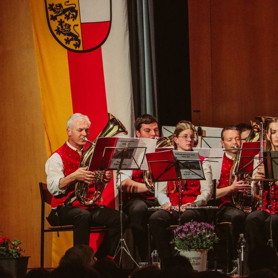 Ein Blechbläserensemble spielt auf der Bühne mit einer Flagge im Hintergrund.