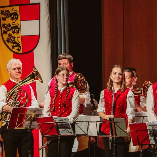 Eine Gruppe von Musikern in roten Westen steht auf der Bühne und spielt. Sie halten Musikinstrumente und lächeln.