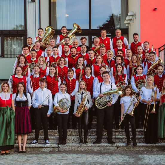 Eine große Gruppe von Menschen in roten und weißen Uniformen, die Musikinstrumente halten und auf einer Treppe für ein Foto posieren.