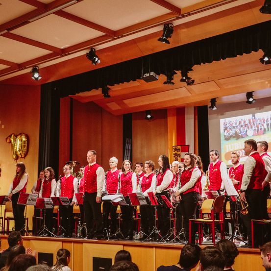 Eine Gruppe von Menschen auf der Bühne, gekleidet in Rot und Weiß, spielt ihre Instrumente vor einem Publikum.
