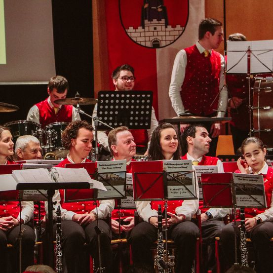 Eine Gruppe von Musikern in roten Westen spielt auf der Bühne vor einem Bildschirm im Hintergrund.