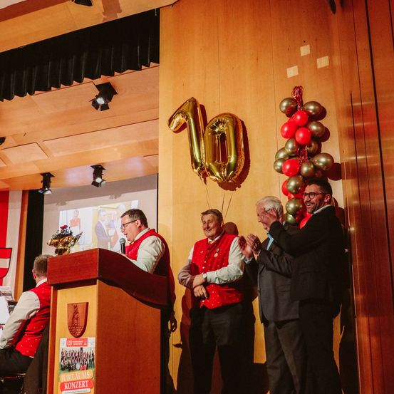 Vier Männer stehen vor einem Podium mit einer großen Ballonzahl 10.