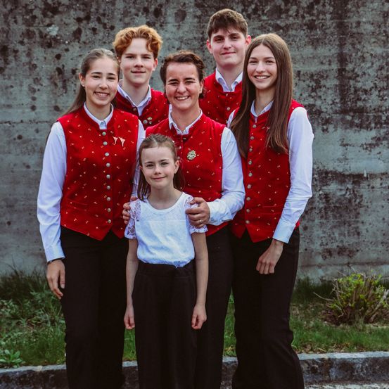 Eine Gruppe von fünf jungen Leuten, in traditioneller Kleidung gekleidet, stehen auf einem Bürgersteig zusammen und lächeln für ein Foto.