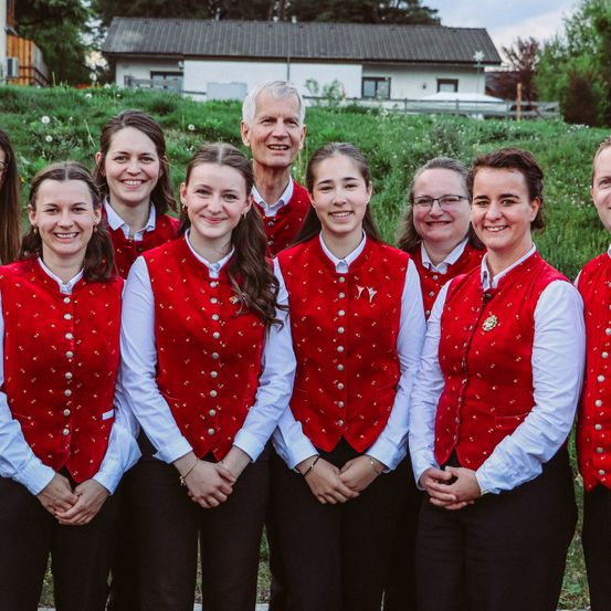 Eine Gruppe von Frauen und ein älterer Mann stehen vor einem Haus mit einem grünen Rasen und lächeln und posieren für ein Foto.