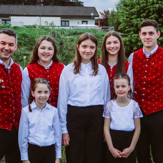 Eine Gruppe von Menschen, möglicherweise eine Familie, steht zusammen im Freien in passender roter und weißer traditioneller Kleidung. Sie lächeln und posieren für ein Foto auf einer Wiese.