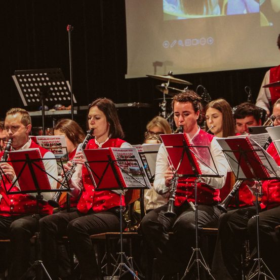 Eine Gruppe von Musikern in roten Westen spielt Klarinetten auf der Bühne mit einem Projektor im Hintergrund.