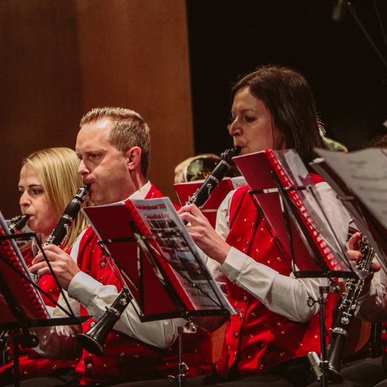 Eine Gruppe von Musikern in roten Westen spielt Klarinetten während einer Aufführung. Sie halten Notenständer mit Notenblättern.