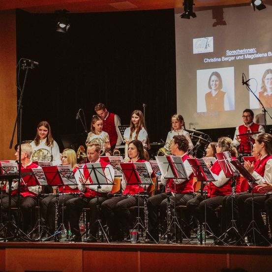 Eine Band spielt auf der Bühne, mit einer großen Leinwand im Hintergrund, die zwei Frauen zeigt.