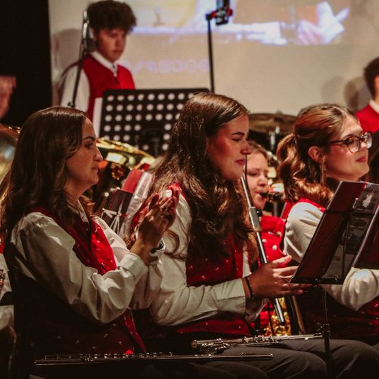Eine Gruppe junger Musiker in passenden roten Westen spielt während einer Aufführung Instrumente. Die Frau rechts konzentriert sich auf ihr Notenblatt.