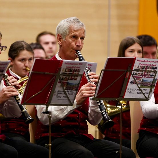 Ein erwachsener Mann spielt Klarinette in einer Band mit anderen Leuten. Die Band spielt, mit Musiknoten auf den Notenständern.