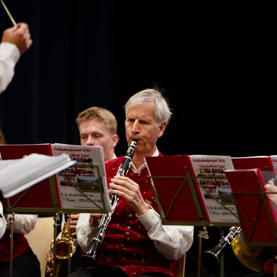 Ein Mann in einem roten Vest spielt Klarinette bei einem Musikkonzert mit einem Saxophonisten und anderen dahinter.