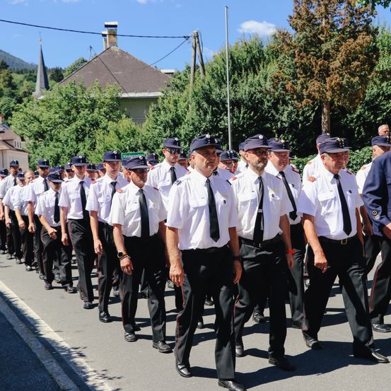 Eine Gruppe uniformierter Personen in Hüten und Krawatten, die bei einem Umzug an einem sonnigen Tag gehen.