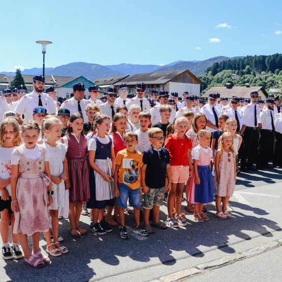 Eine Gruppe von Kindern in bunter Kleidung posiert für ein Foto in einer Stadt mit Bergen im Hintergrund.
