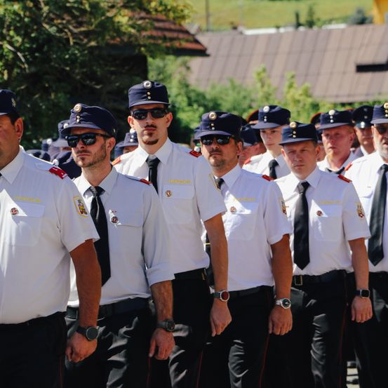 Eine Gruppe uniformierter Männer, wahrscheinlich Polizisten, steht in einer Reihe draußen. Sie tragen Hüte, Krawatten und Uhren. Sie nehmen wahrscheinlich an einer Parade teil.