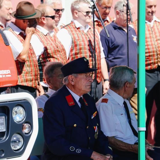 Eine Gruppe von Menschen in Militäruniformen steht in einer Reihe, während ein Mann in Uniform auf einem Stuhl sitzt.