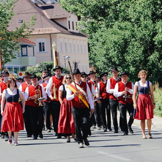 Eine Gruppe von Musikern in traditioneller Kleidung, die in einer Parade marschiert und Blech- und Holzblasinstrumente trägt, unter einem klaren Himmel.
