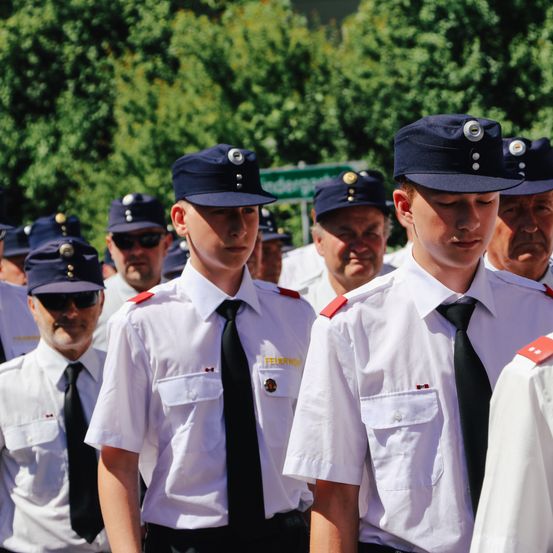 Eine Gruppe uniformierter Männer steht bei einer Parade zusammen und trägt Knöpfe und Krawatten an ihren Mützen. Sie sind wahrscheinlich Polizisten, die in einer Reihe nach vorne schauen.