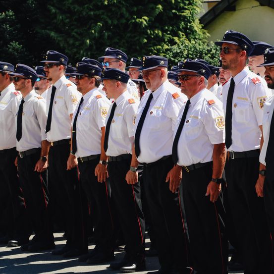 Eine Reihe uniformierter Offiziere, möglicherweise Polizisten, stehen in einer Reihe draußen. Sie tragen Hüte und Brillen. Sie tragen schwarze Krawatten und Gürtel mit roten Streifen an den Hosen.