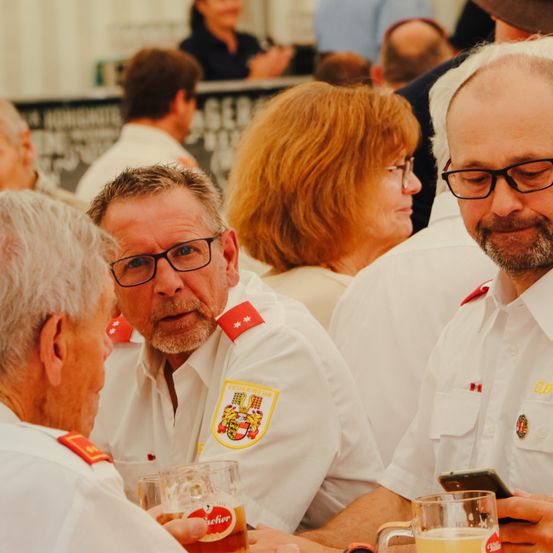 Eine Gruppe von Feuerwehrleuten in Uniform, einschließlich zwei Männern und einer Frau, sitzen zusammen und genießen Getränke.