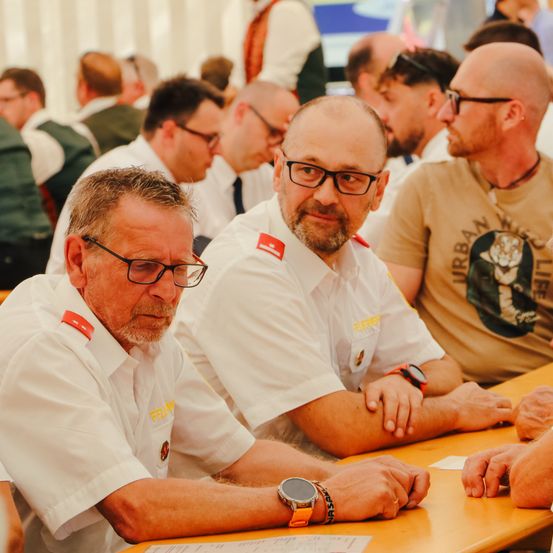 Mehrere Männer in Uniformen sitzen an einem Tisch mit Papieren. Einige tragen Brillen und einer hat eine Uhr. Sie sehen konzentriert aus und sind in eine Diskussion vertieft.