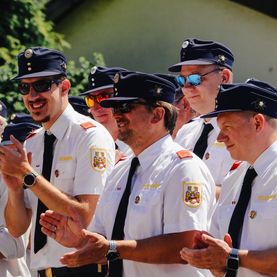 Eine Gruppe uniformierter Personen, wahrscheinlich Polizisten, steht draußen. Sie lächeln, klatschen und tragen Mützen mit Abzeichen.