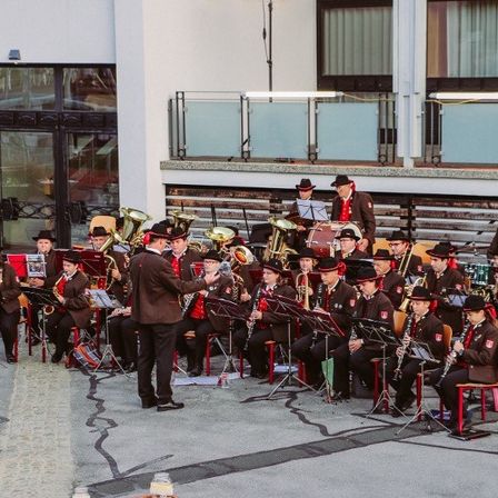 Eine Brass Band spielt vor einem Gebäude mit Glasfenstern und Balkon.