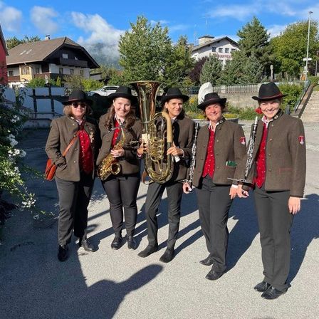 Fünf Personen stehen auf der Straße und posieren für ein Foto. Sie tragen alle Hüte und Mäntel. Vier von ihnen halten Musikinstrumente in den Händen.