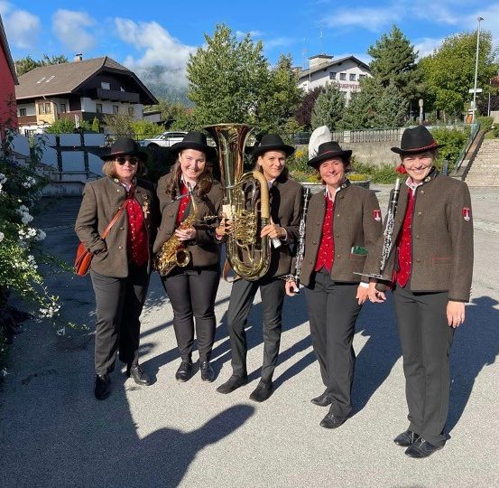 Fünf Personen stehen auf der Straße und posieren für ein Foto. Sie tragen alle Hüte und Mäntel. Vier von ihnen halten Musikinstrumente in den Händen.