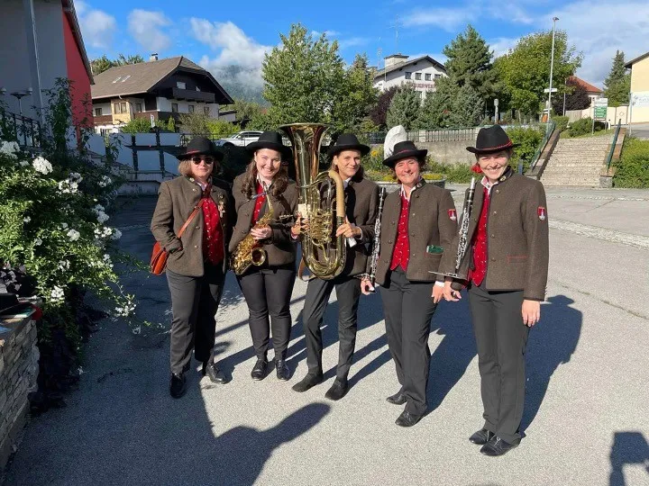 Fünf Personen stehen auf der Straße und posieren für ein Foto. Sie tragen alle Hüte und Mäntel. Vier von ihnen halten Musikinstrumente in den Händen.