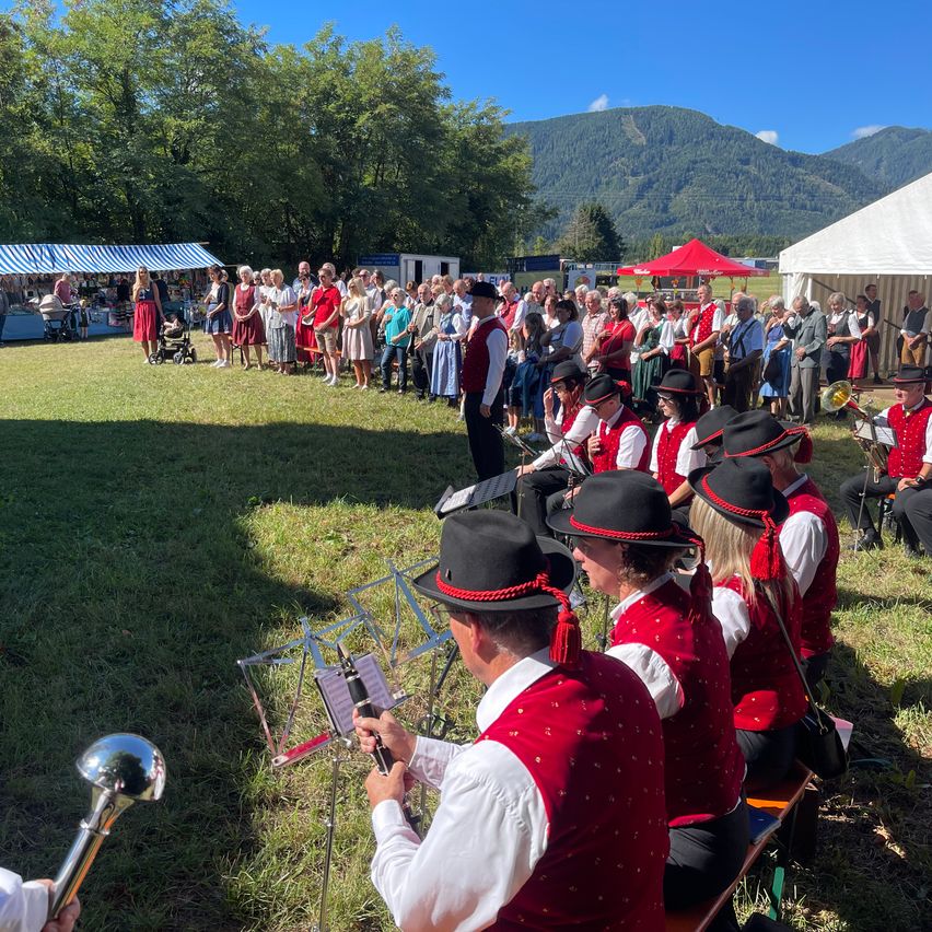 Eine Gruppe von Menschen in traditioneller Kleidung spielt Musik an einem Ort im Freien mit Bergen im Hintergrund.