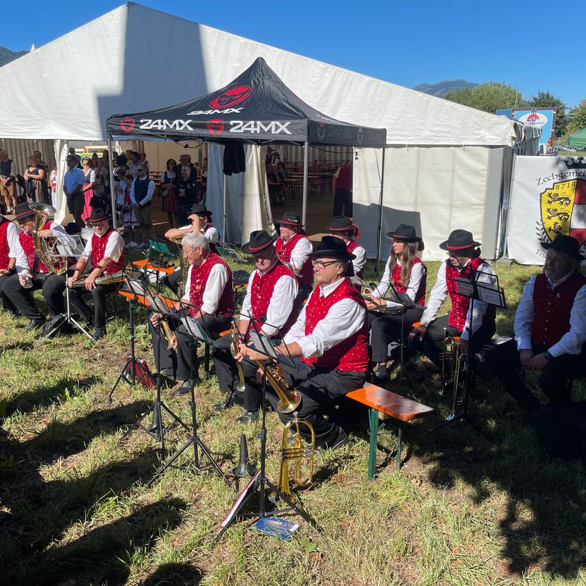 Eine Gruppe von Musikern in roten Westen und schwarzen Hüten spielt Instrumente unter einem Zelt, während eine Menge im Hintergrund zuschaut.