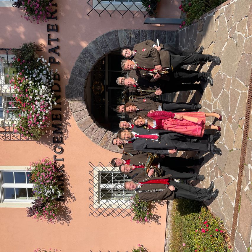 Eine Gruppe von Musikern posiert für ein Foto vor einem Gebäude mit Blumen, das Gasthof Meierei heißt. Sie halten verschiedene Musikinstrumente.