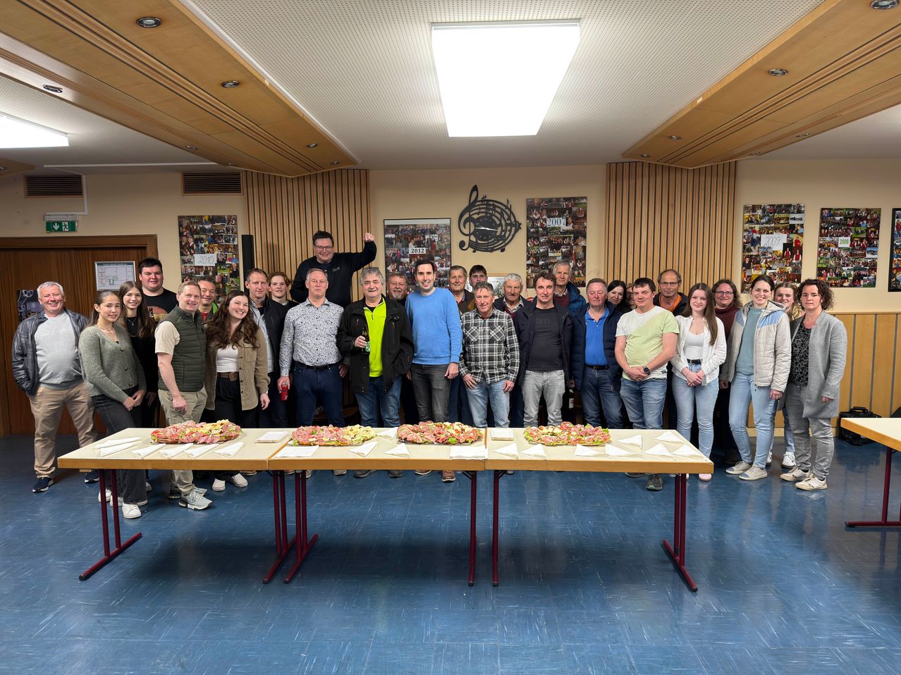 Eine Gruppe von Menschen posiert für ein Foto in einem Raum mit gedeckten Tischen, einige lächeln und ein Mann steht auf einem Tisch.