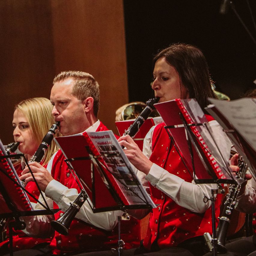 Vier Musiker spielen auf der Bühne und tragen alle rote Westen. Der Mann in der Mitte spielt Klarinette, während die Frau neben ihm ebenfalls Klarinette spielt.