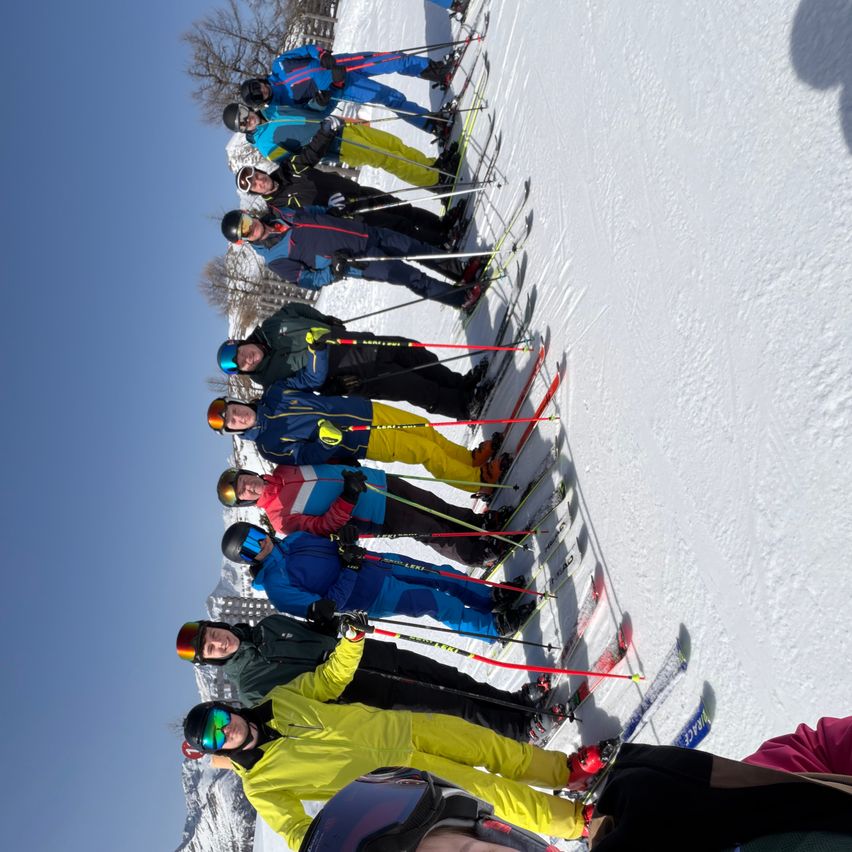 Eine Gruppe von Skifahrern in verschiedenen farbigen Outfits und Helmen posiert für ein Foto auf einer verschneiten Piste.
