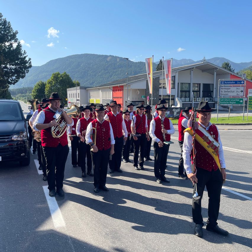 Eine Blaskapelle in roten Westen und schwarzen Hüten spielt Instrumente bei einer Parade an einem sonnigen Tag.