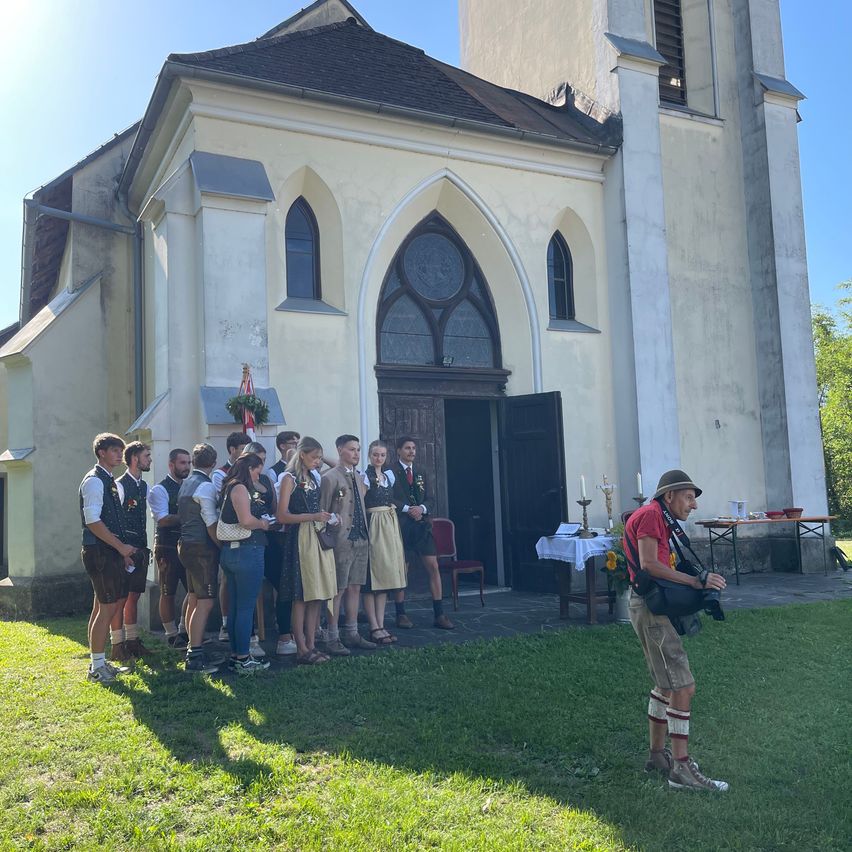 Eine Gruppe von Menschen in traditioneller Kleidung steht vor einer Kirche, während ein Mann ein Foto macht.