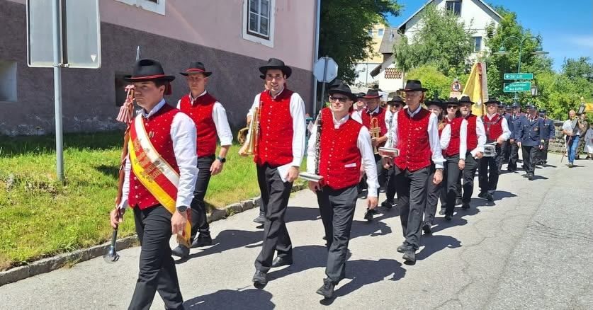 Eine Gruppe von Männern in traditioneller Kleidung marschiert eine Straße hinunter und spielt verschiedene Musikinstrumente.