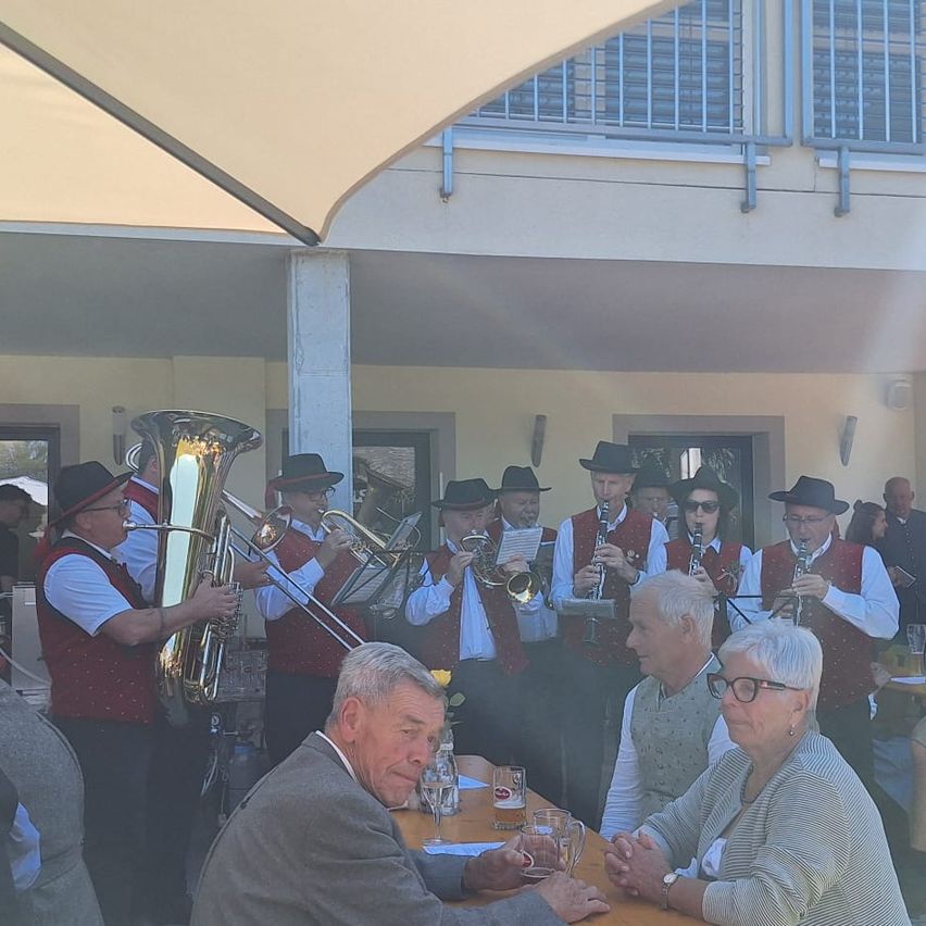 Eine Gruppe von Musikern in traditioneller Kleidung spielt Instrumente im Freien, mit einem Paar, das vorne an einem Tisch sitzt.