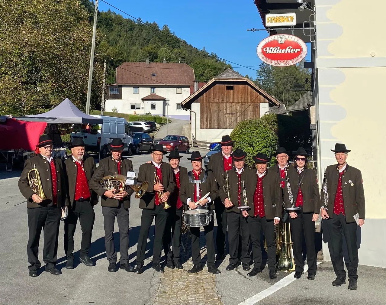 Eine Gruppe von Musikern in traditioneller Kleidung posiert für ein Foto vor einem Gebäude mit einem Schild, das 'Villacher' liest.